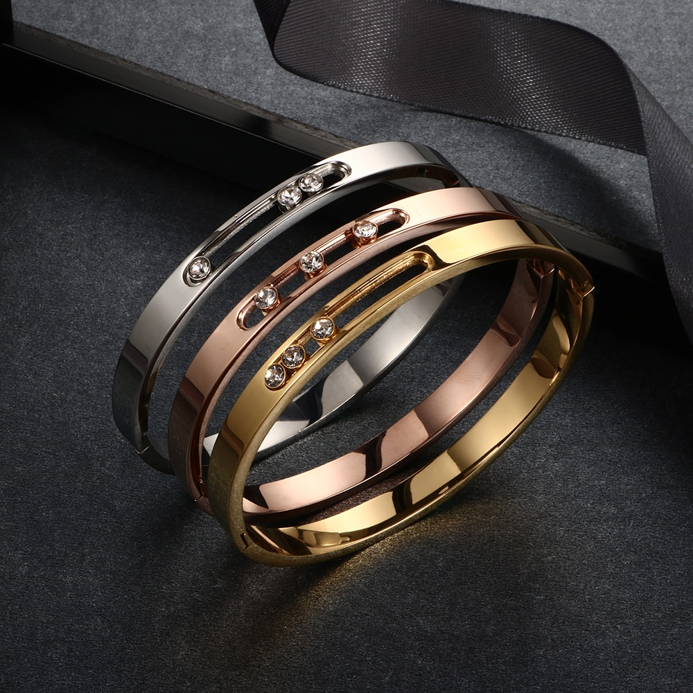 Three metallic rings in gold, rose gold, and silver on a dark surface with a black ribbon. designer inspired by messika